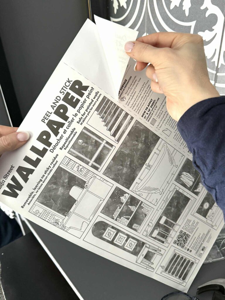 Peeling the back of a dollar store sheet of peel-and-stick wallpaper.