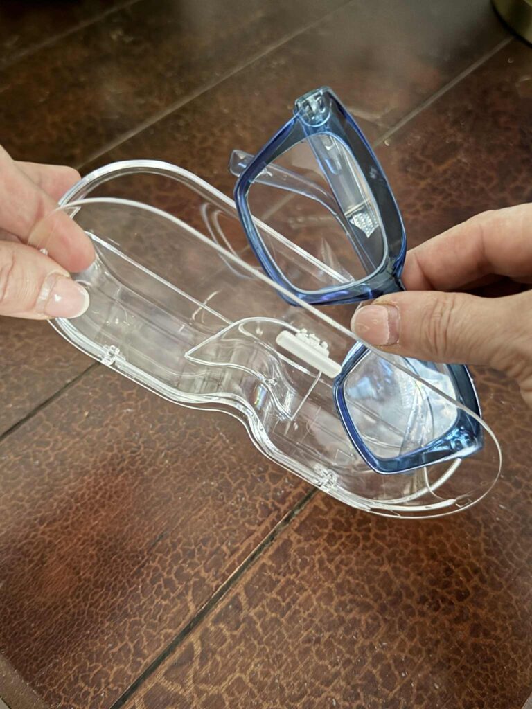 how to organize sunglasses: A pair of blue reading glasses be placed in a clear acrylic storage case.