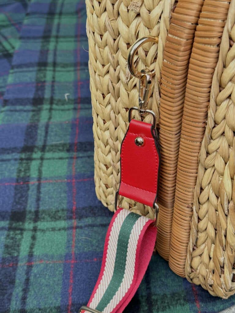 A purse guitar strap hooked onto an O ring on the side of a picnic basket.