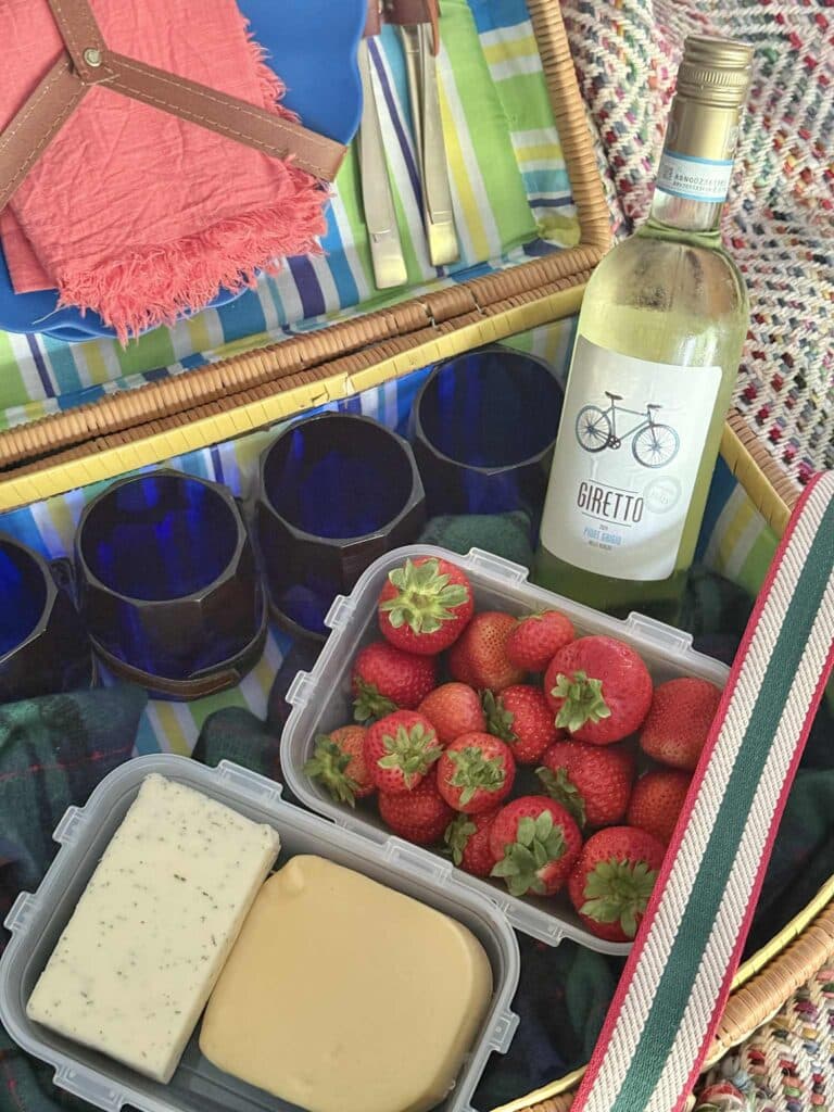 A bottle of wine, strawberries, and cheese inside a picnic hamper.