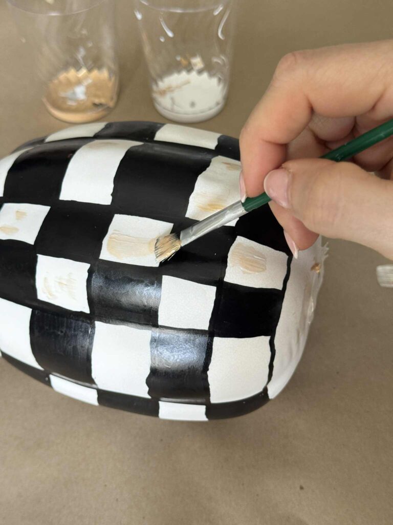 Adding faint gold brush marks to a checkered pumpkin DIY.