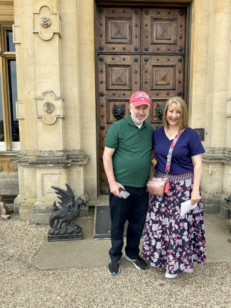 A man and woman standing in front of the wood doors of Highclere Castle for a Downton Abbey Tour.