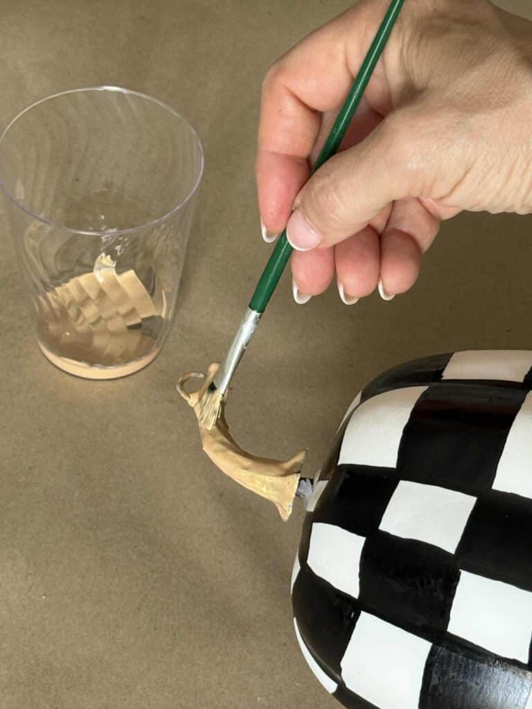 Painting a pumpkin stem with gold paint.