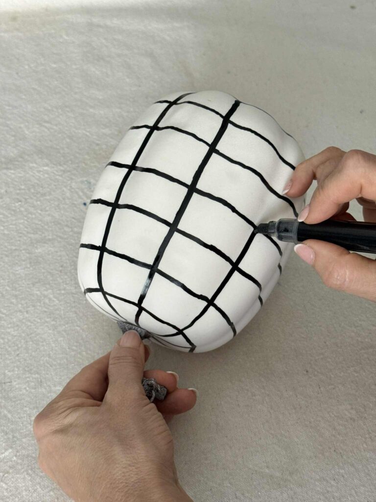 Painting vertical lines on a faux pumpkin to create a checkerboard pattern.