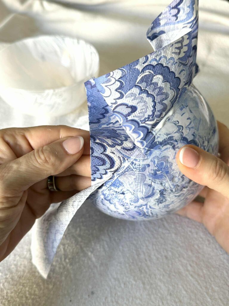 Pressing a patterned paper napkin to the inside of a clear ornament ball with glue.