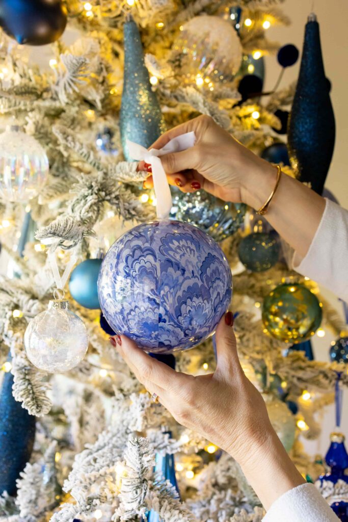 Hanging a blue decoupage ornament on a Christmas tree.