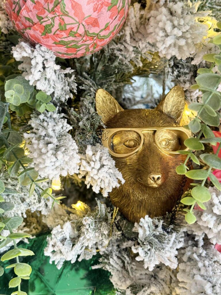 A brass woodland fox tucked into a decorated flocked Christmas tree.