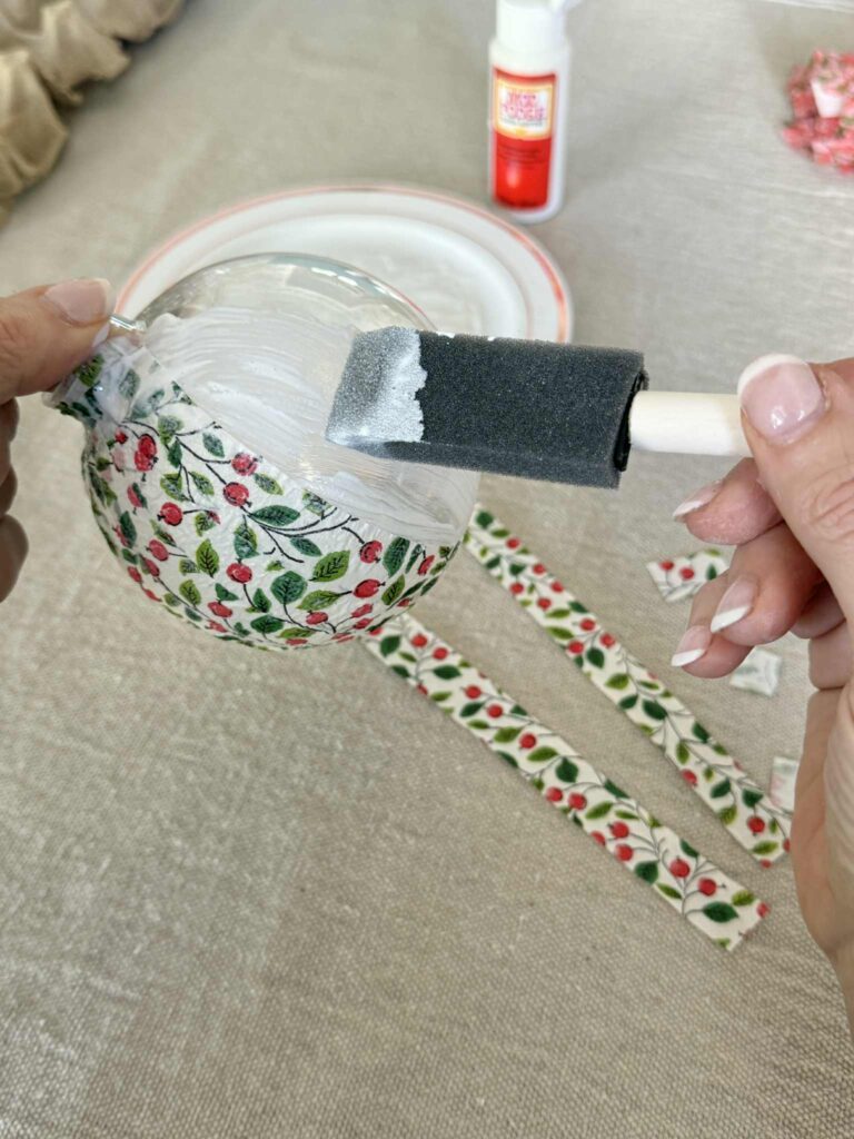 Brushing decoupage glue onto a clear ornament ball.