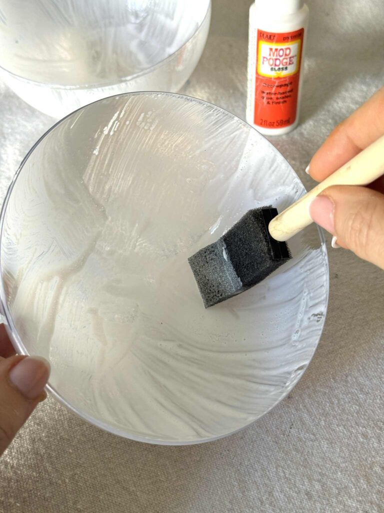 Brushing decoupage glue to the inside of a clear Christmas ornament ball.