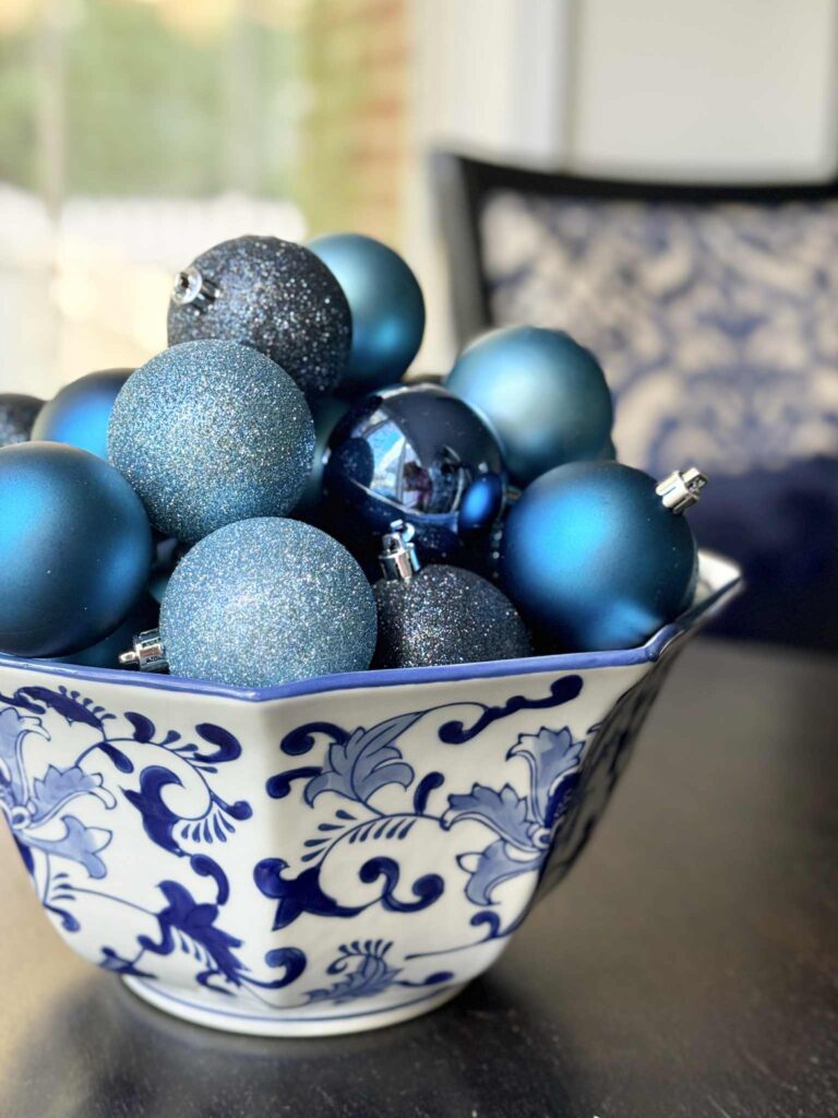 A chinoiserie bowl full of Christmas ornaments in shades of blue.
