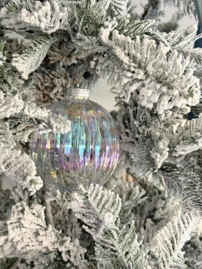 A clear ornament ball decorating a flocked Christmas tree.