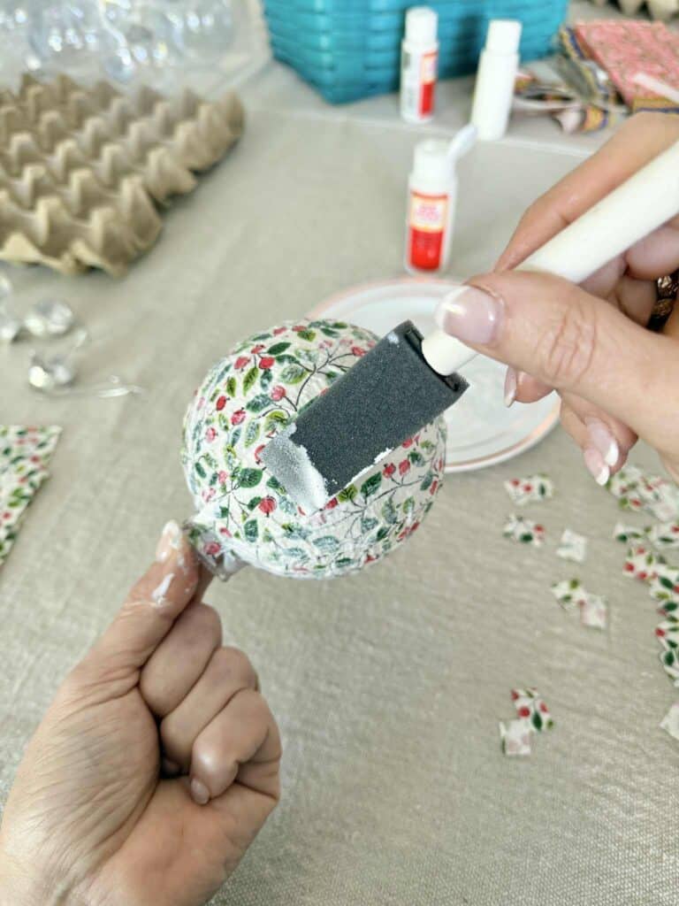Brushing decoupage glue over the outside of an ornament ball.