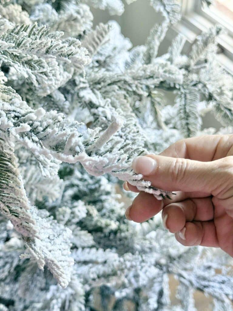 A woman's hand holding the branch of a flocked Christmas tree.