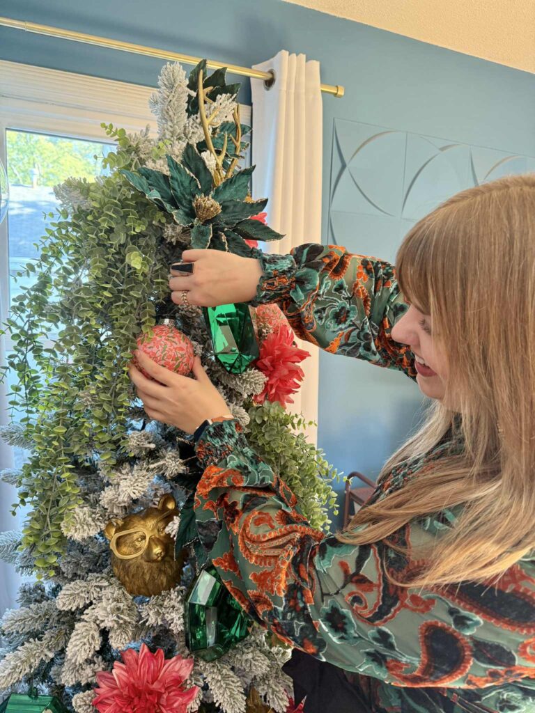 A woman hanging a DIT decoupage ornament decoration on a flocked Christmas tree.