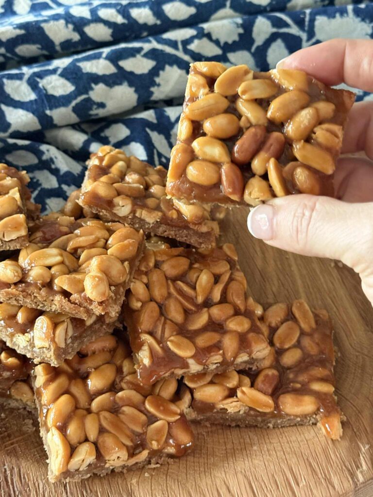 A hand holding a salted peanut cookie bar next to a pile of bars.