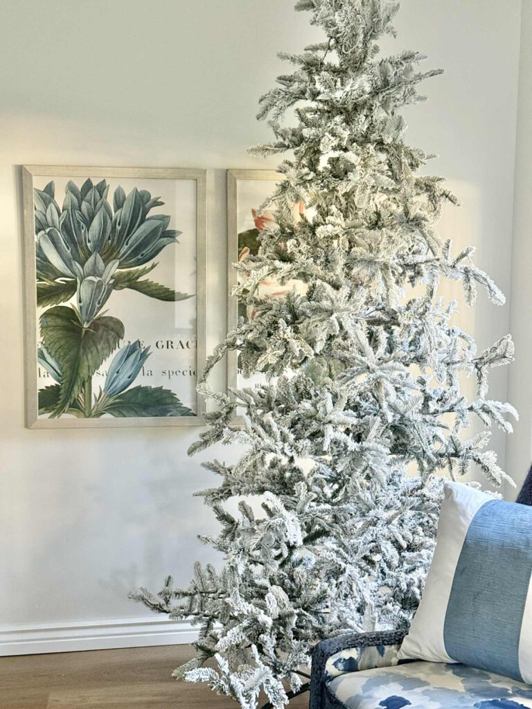 Decorating Ideas for a flocked Christmas tree: A King of Christmas flocked tree in a bedroom with a blue botanical on the wall.