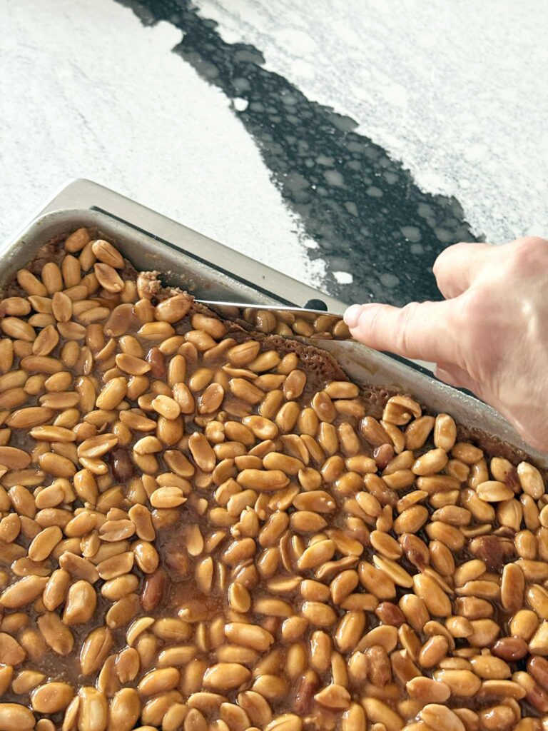 Loosening the edges of baked salted peanut bars from the side of the pan.