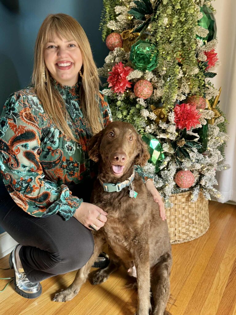 A woman and dog sitting in front of a decorate flocked Christmas tree.