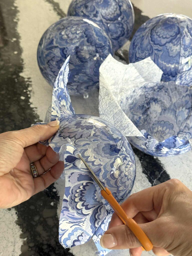 Trimming the excess paper napkin from half of a clear ornament ball.