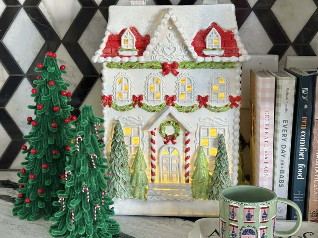pipe cleaner Christmas trees sitting beside a Christmas tabletop house.