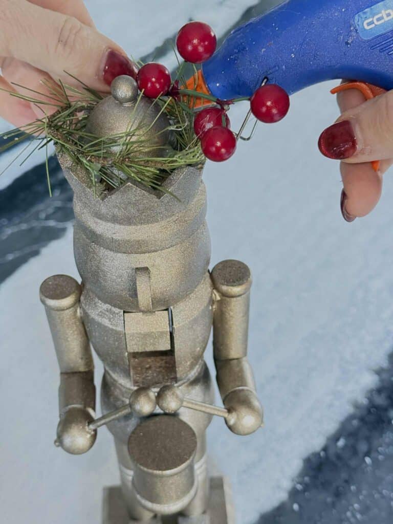 Gluing red berries into the crown of a painted wood nutcracker for Christmas.