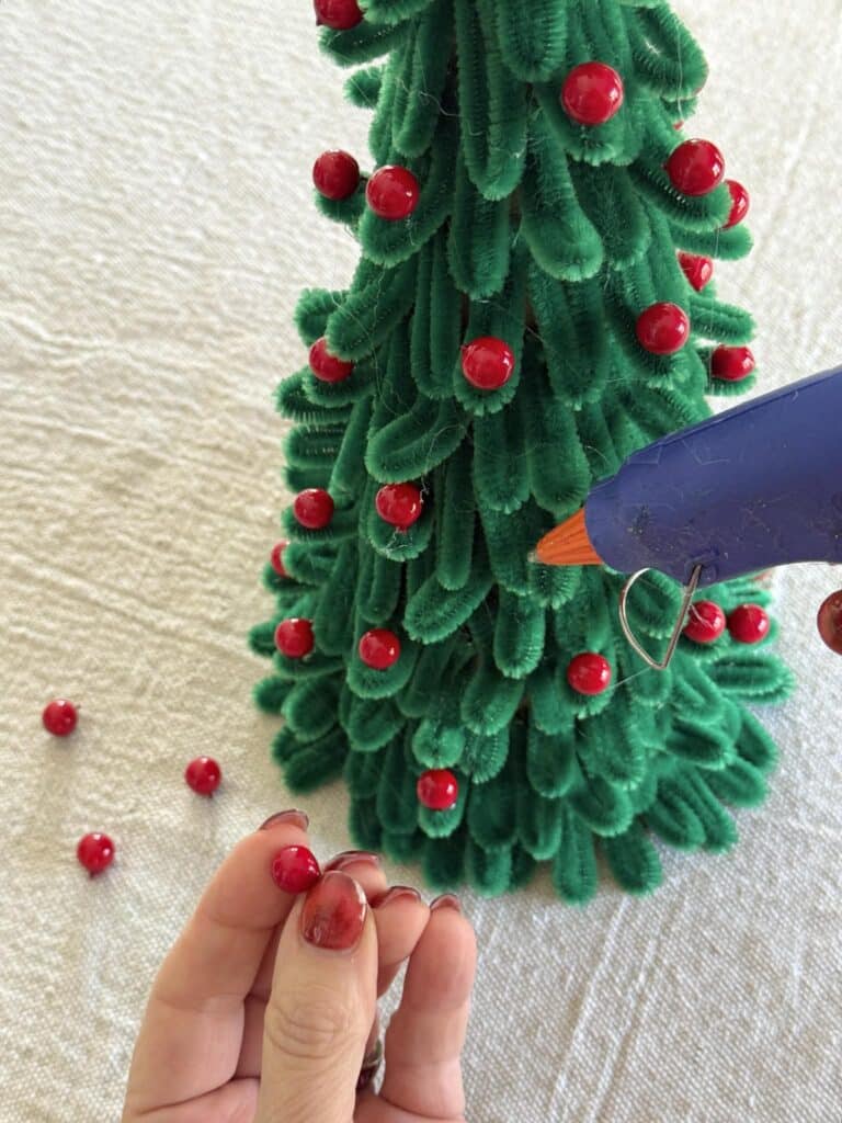 Gluing red berries onto a pipe cleaner Christmas tree.