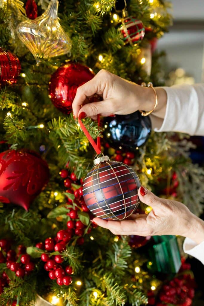 Woman's hand hanging a red plaid ornament on a Ralph Lauren Christmas tree.