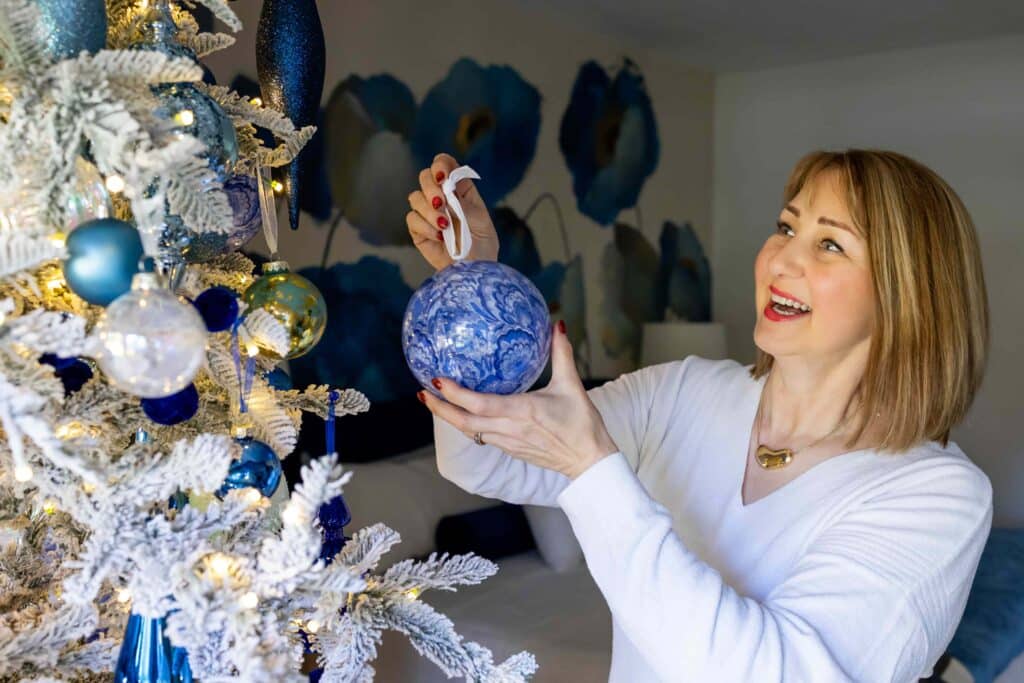Woman hanging a blue and white ornament on a flocked Christmas tree.