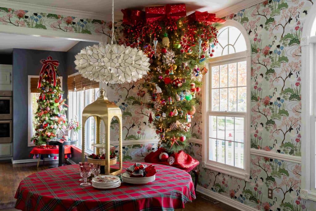A Christmas tree in a dining room with a kitchen Christmas tree in the distance.