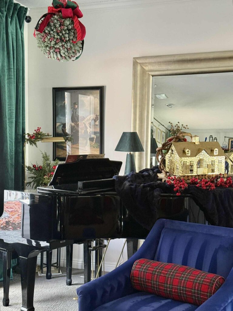 Piano decorated for Christmas with gold carriage house, kissing ball, and greenery.
