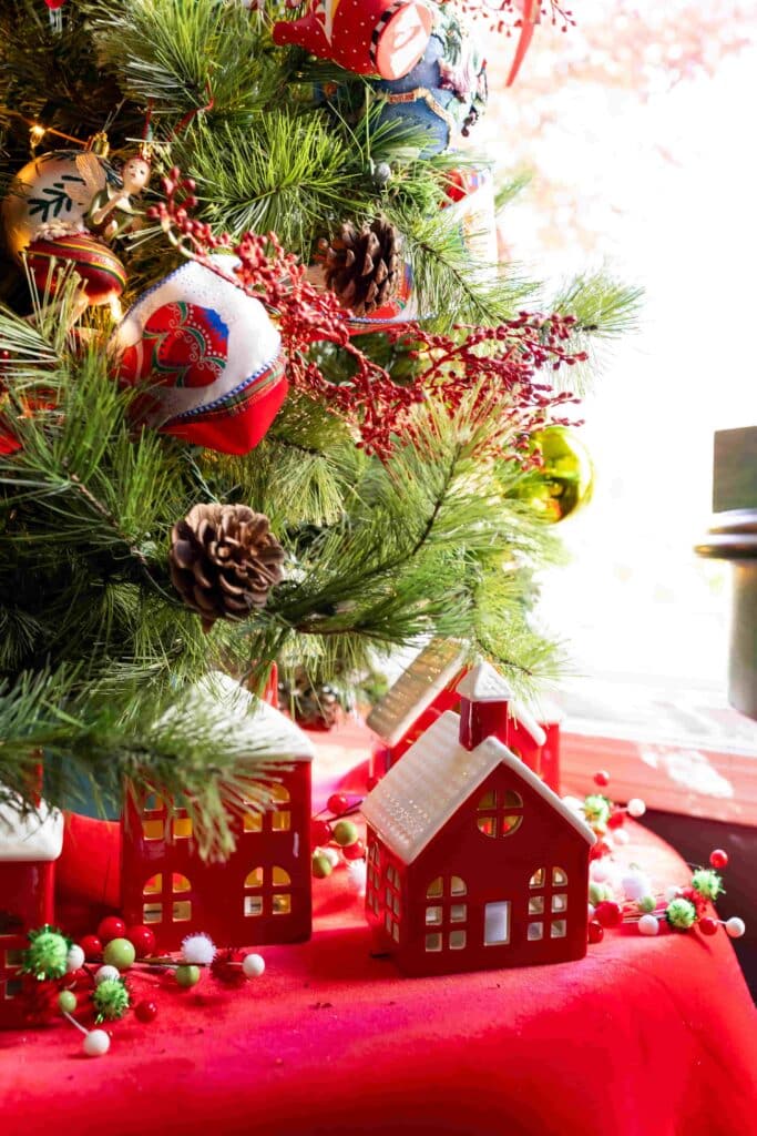 A red ceramic Christmas village sitting at the base of a decorated Christmas tree.