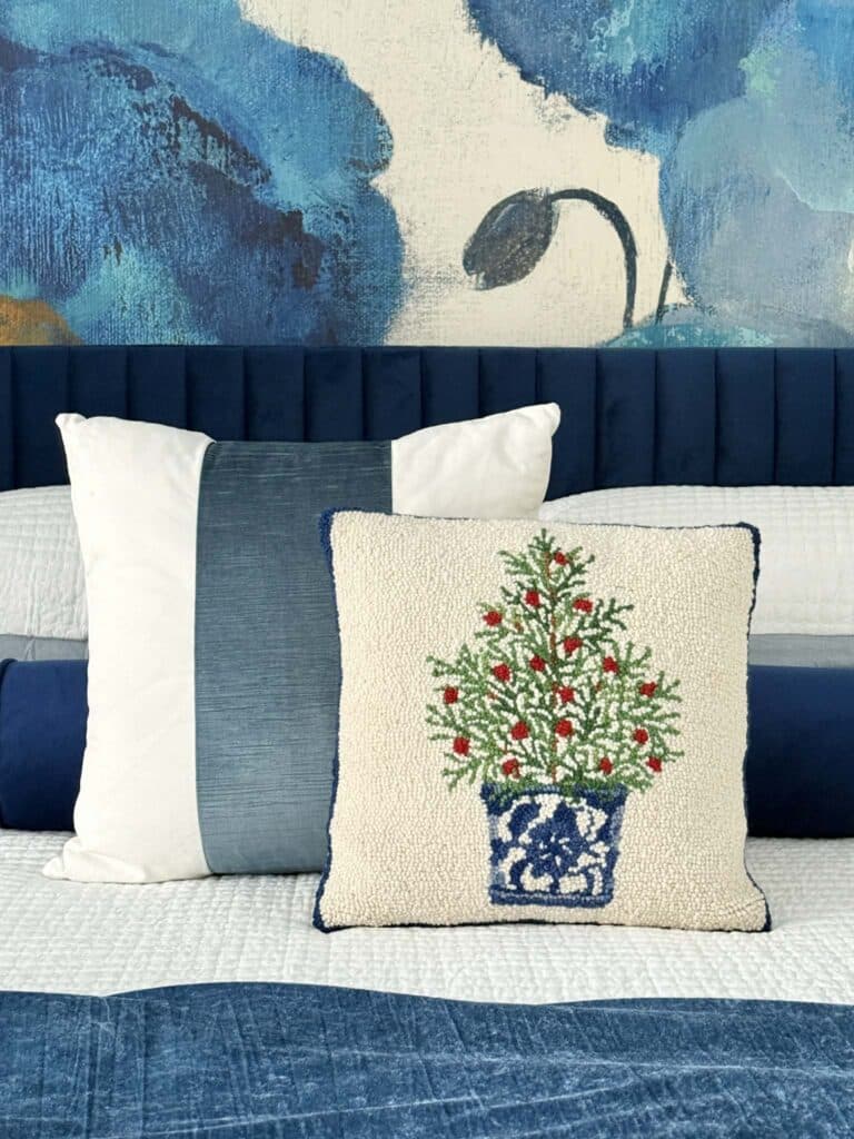 A Christmas pillow with a tree design decorating a bed.