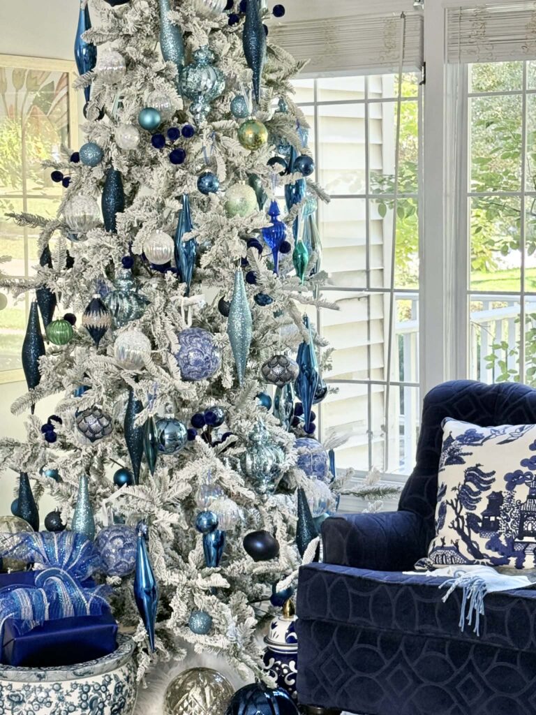 A flocked white Christmas tree decorated with ornaments in shades of blue.
