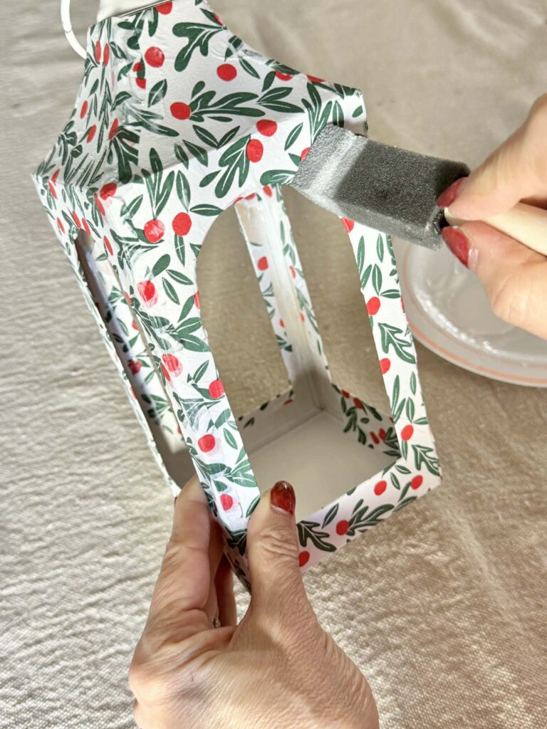 Brushing a final coat of decoupage glue over a DIY Christmas lantern.