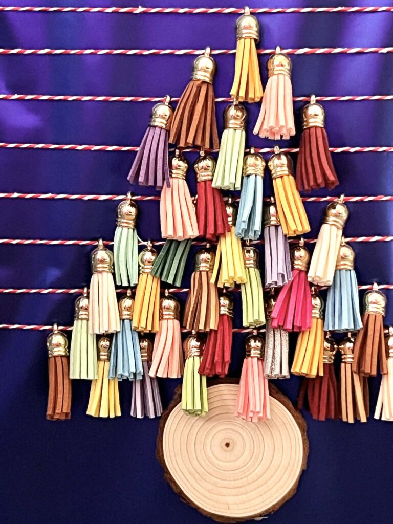 Mini tassels arranged in the shape of a tree on the front of a Christmas gift.