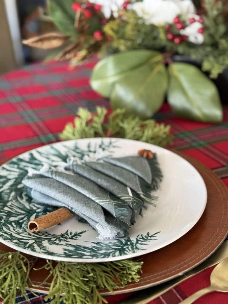 A Christmas tree napkin fold sitting on a plate on a holiday table.
