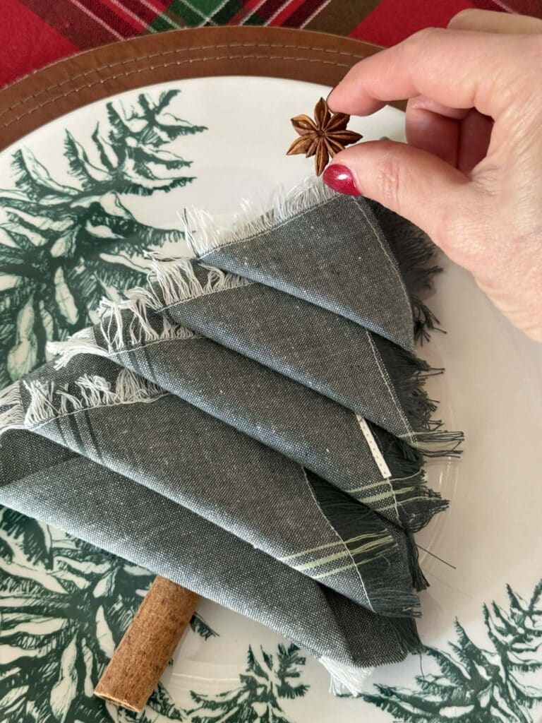Placing star anise on the top of a Christmas tree napkin fold.