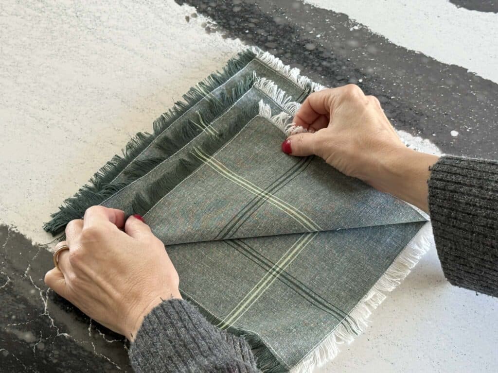 Folding the third tier of a cloth napkin for a Christmas napkin fold.
