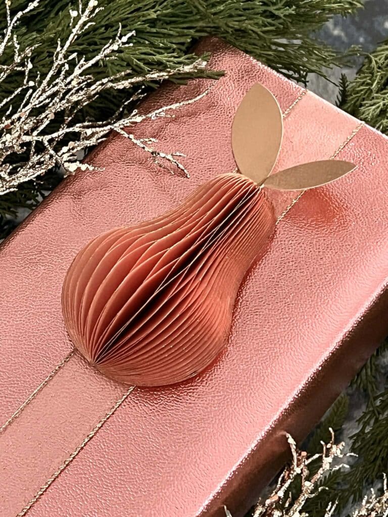A Christmas gift wrapped with tonal paper and ribbon with a 3D Pear ornament affixed to the front.