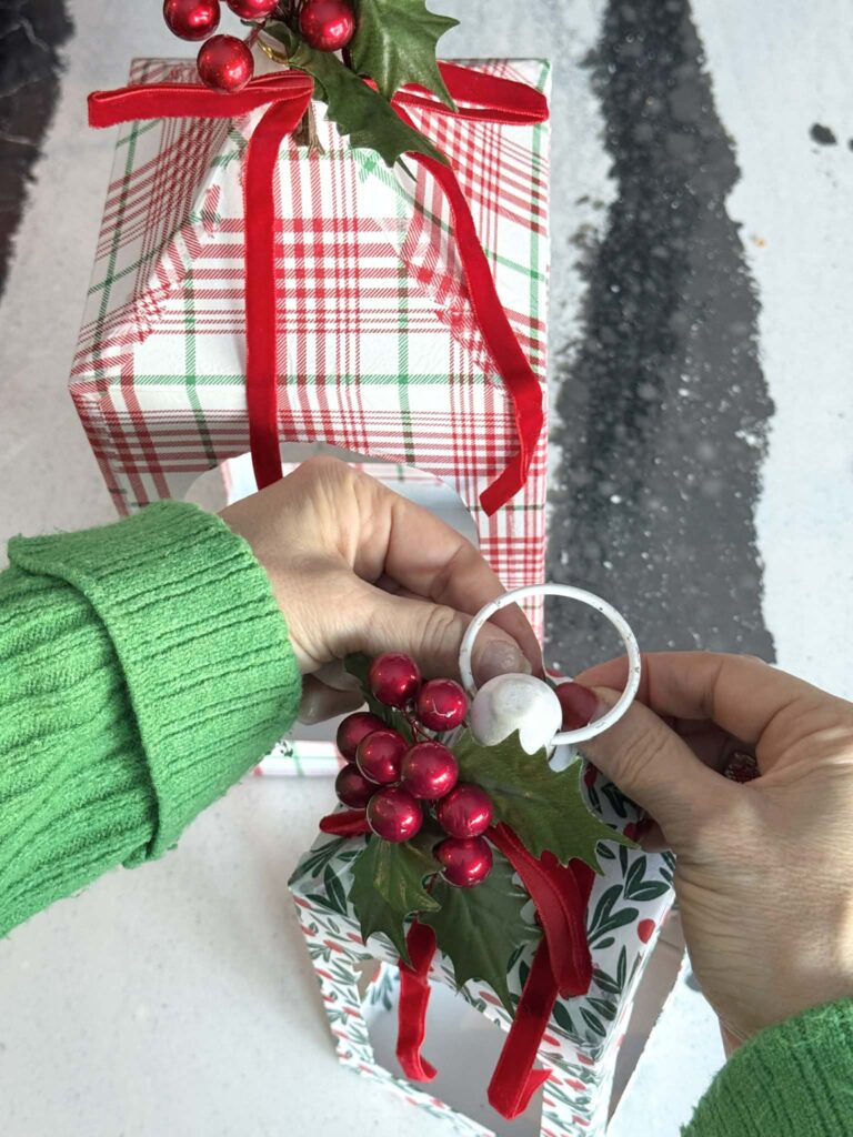 Attaching greenery and red berries to a DIY decoupage Christmas lantern.