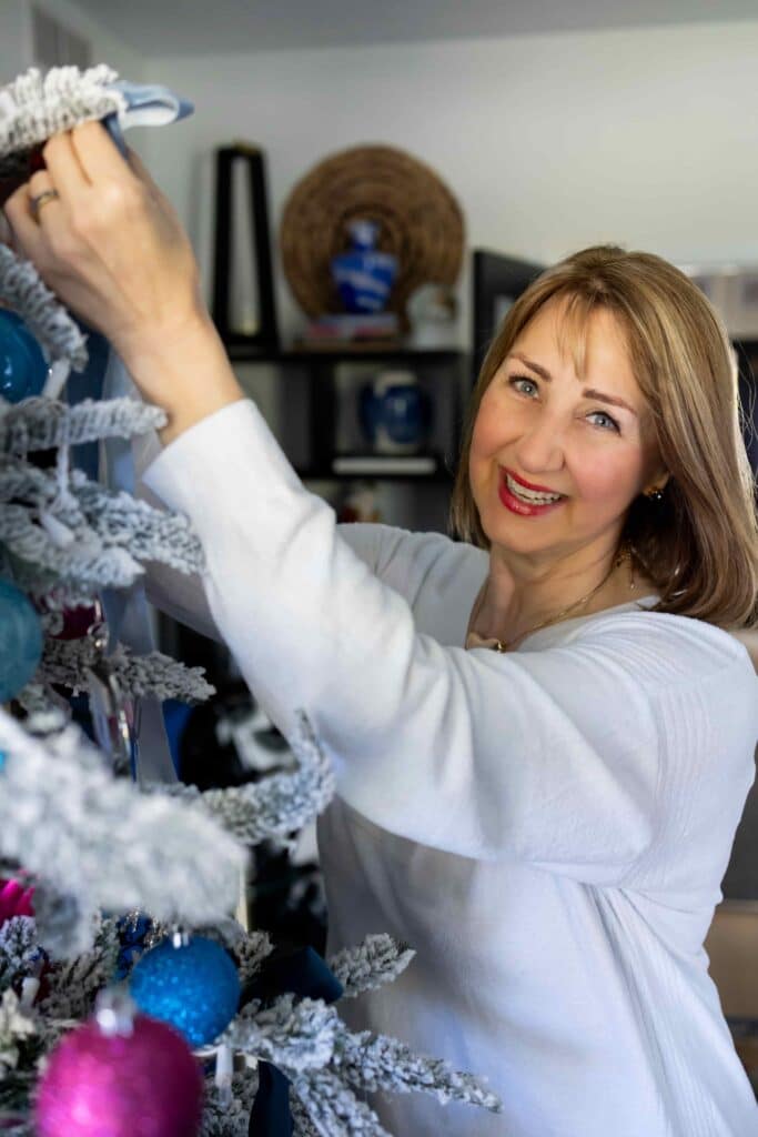 Woman decorating a flocked Christmas tree with blue ornaments.