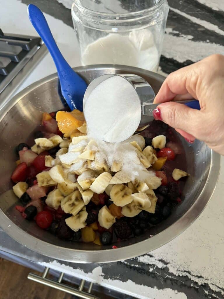 Adding sugar to a bowl of mixed fruit.