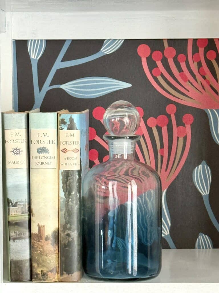 What to Put in a Decanter: using a blue decanter as a bookened on a bookshelf.