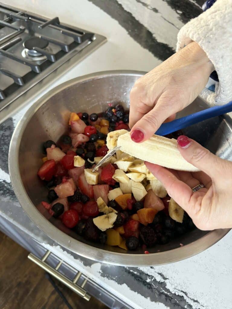 Slicing bananas into a bowl of mixed fruit.