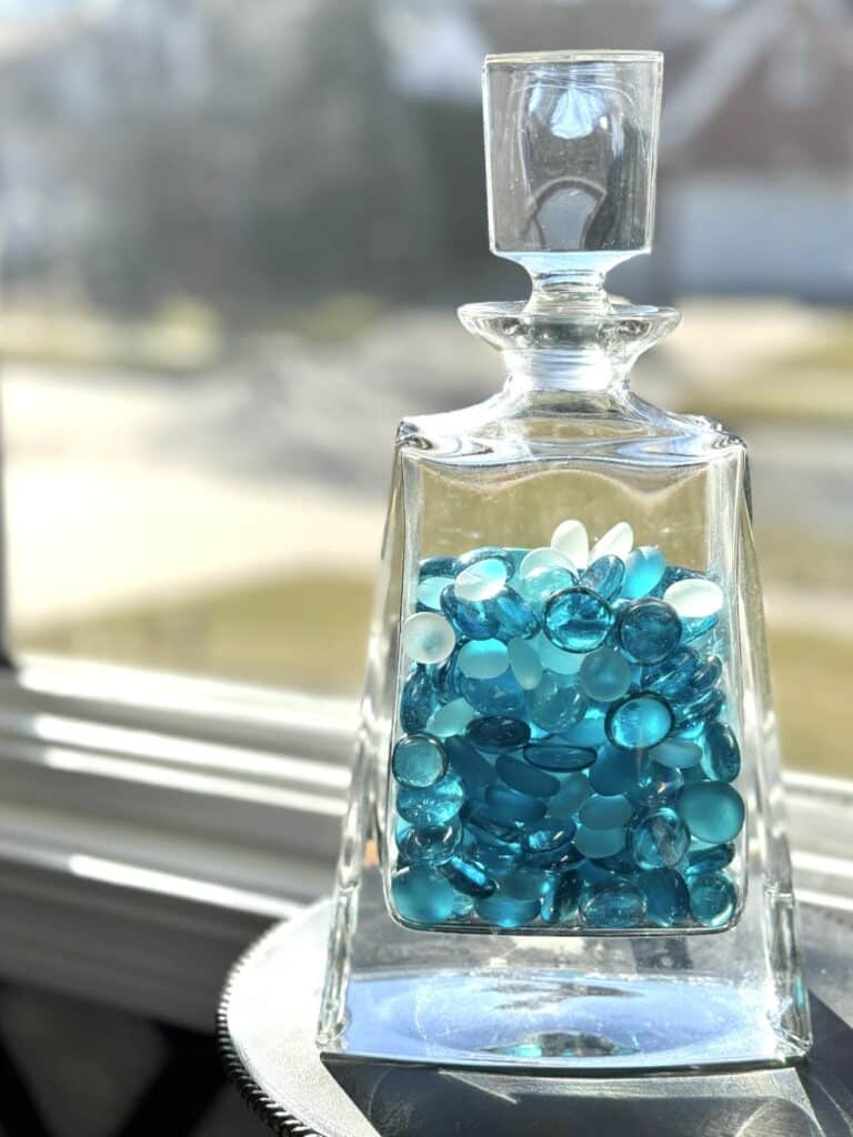 What to Put in a Decanter: blue glass stones in a decanter by a window.