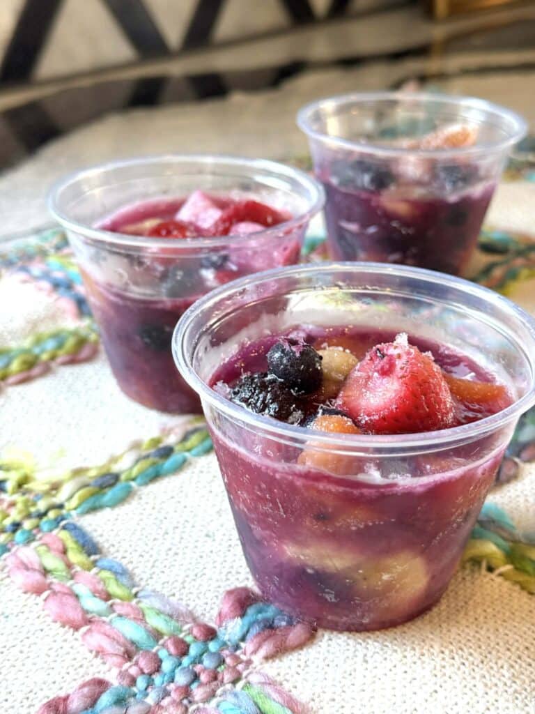 Three frozen fruit cups thawing on a table.