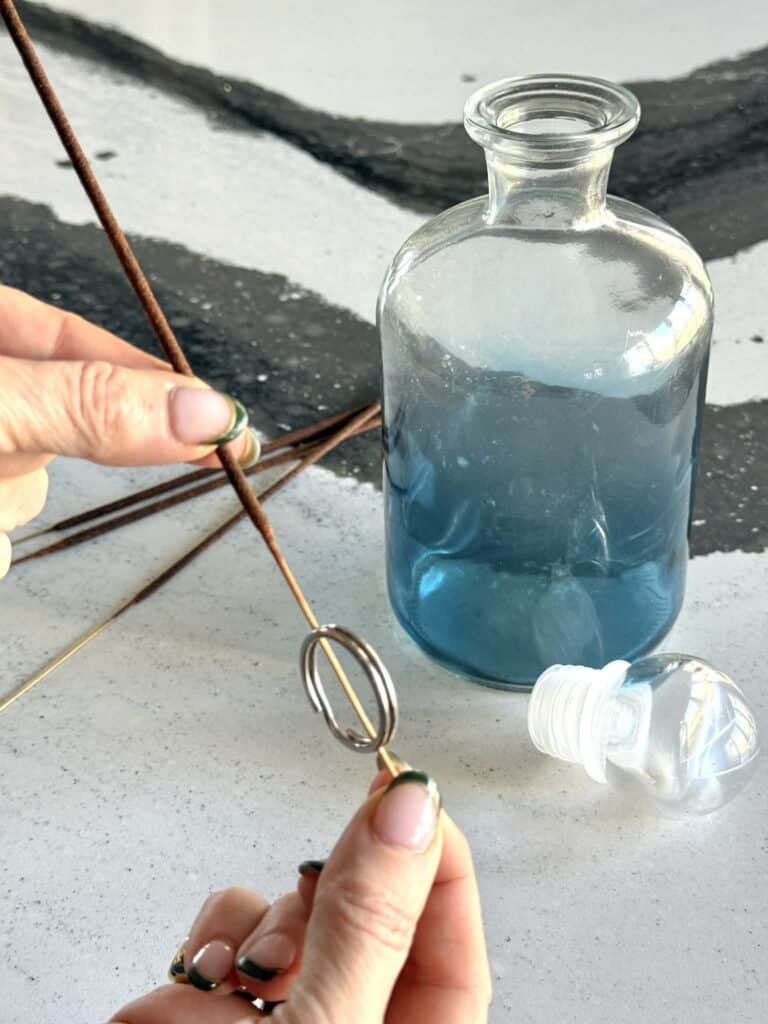 A key ring pressed on the end of an incense stick beside a glass decanter.