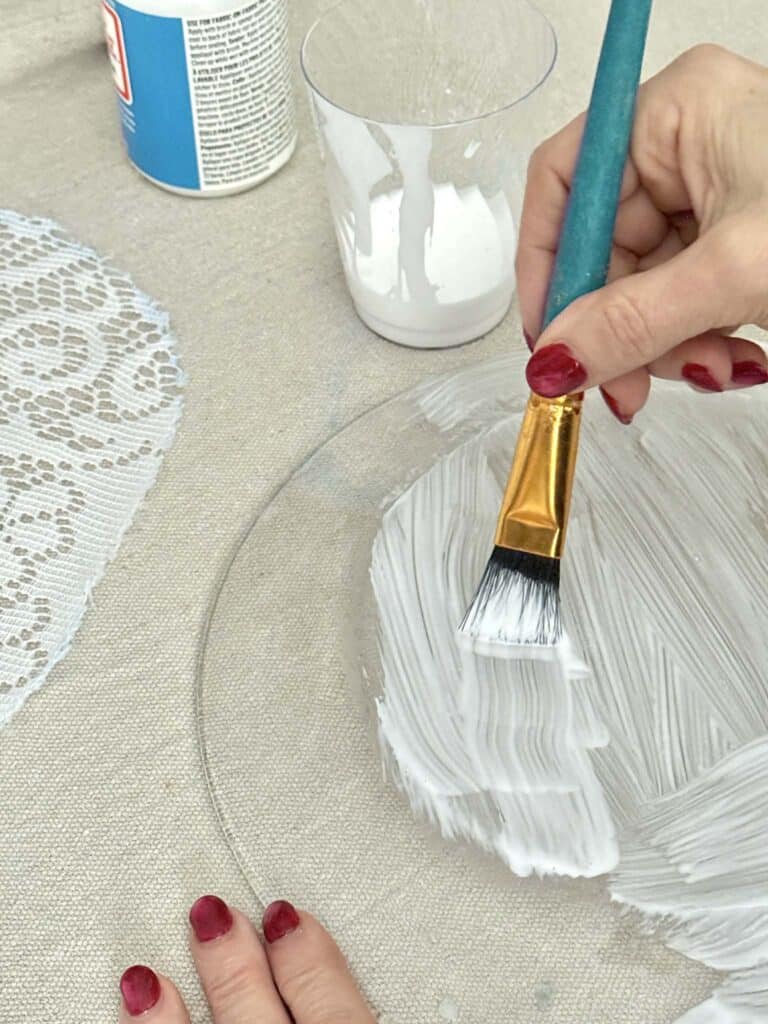Brushing decoupage glue on the back of a glass plate.