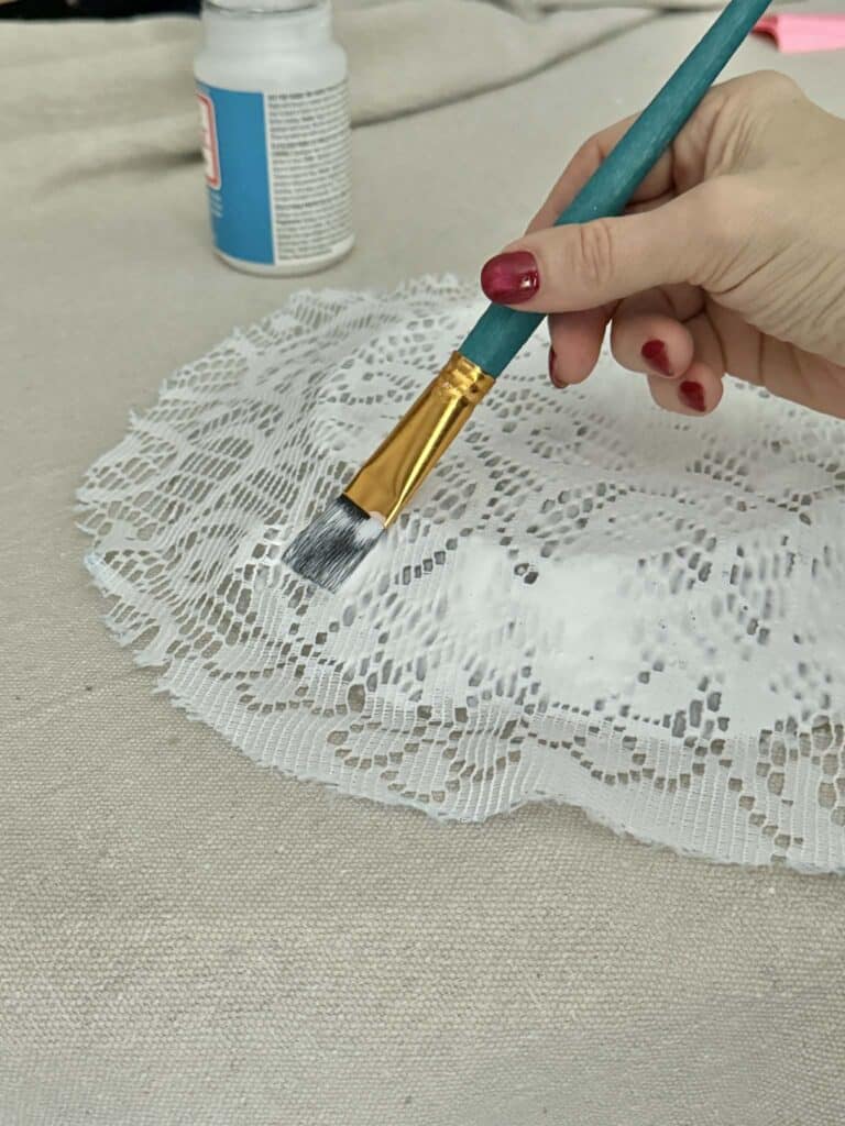 Brushing decoupage glue onto the backside of a lace covered plate.