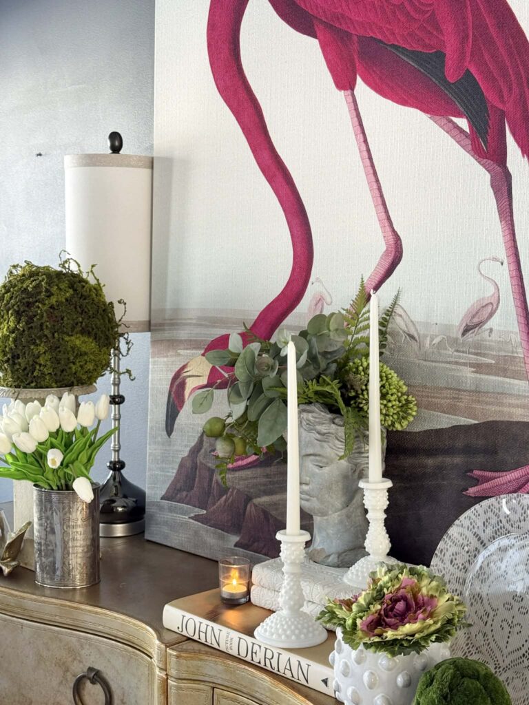 A design vignette consisting of a female bust, white candles, white tulips, and bird wall art.